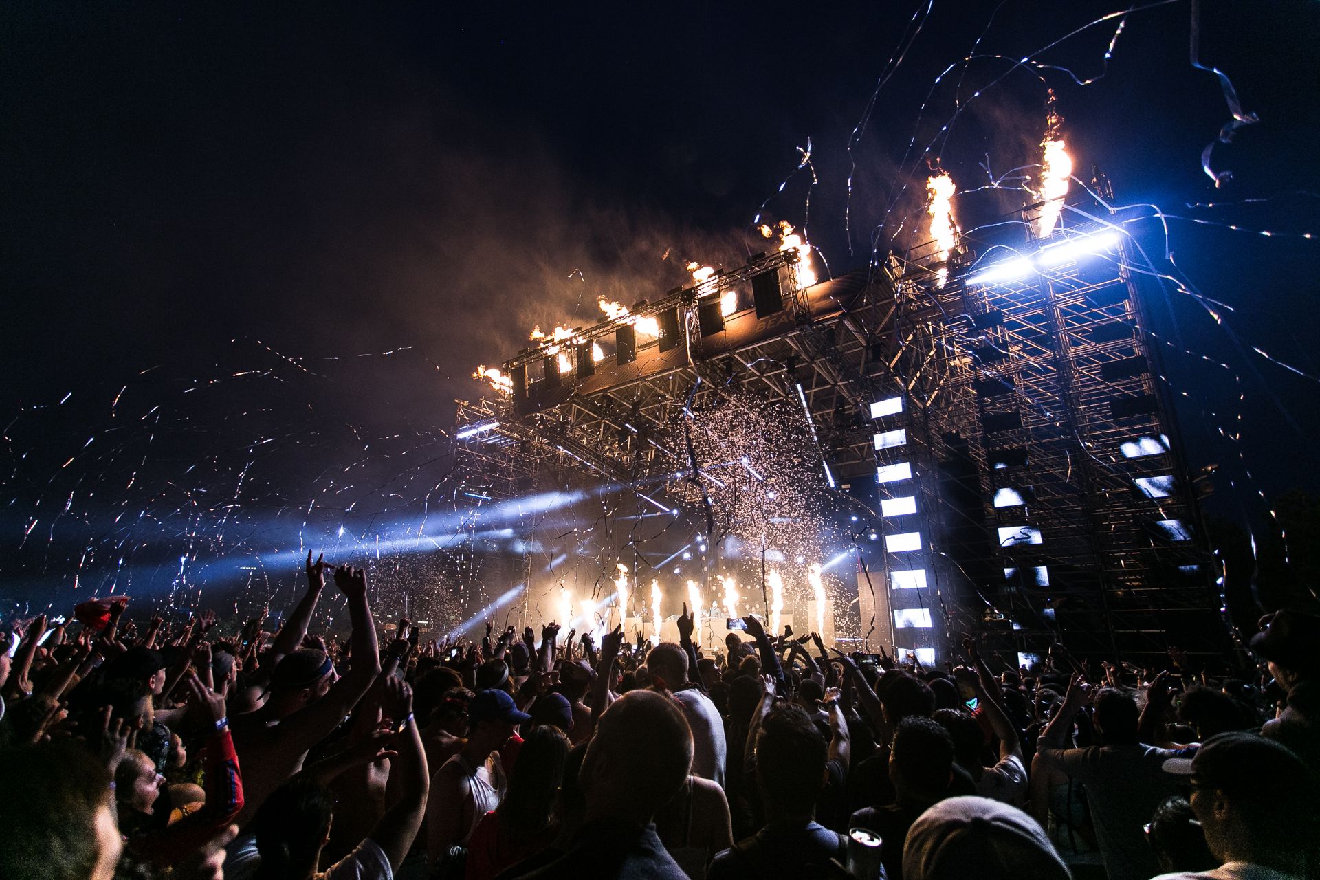 Crowd at a large night-time event with stage pyrotechnics