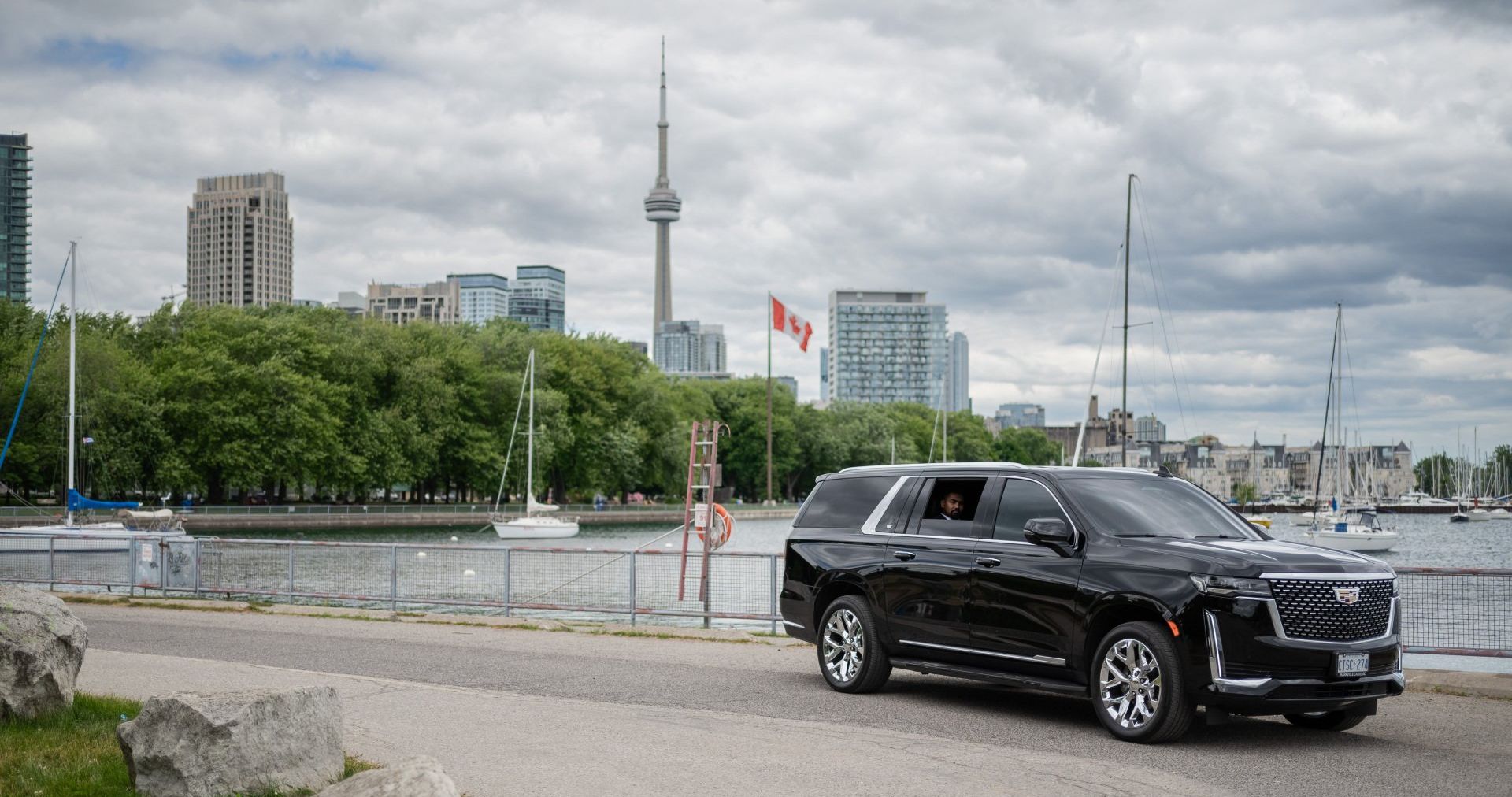 A black executive SUV on the Toronto waterfront, the CN Tower and Canadian flag behind it